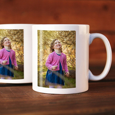 Two mugs with a photo on them of a girl dressed in pink and blue looking at trees, the mugs are sat on a table.