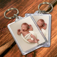 Two keyrings containing a photo of a baby yawning on a wooden tabletop.