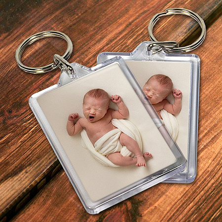 Two keyrings containing a photo of a baby yawning on a wooden tabletop.