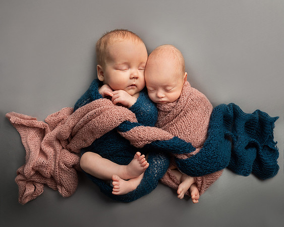 Two babies are wrapped in intertwining blue and pink blankets