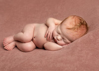 Newborn baby girl lays on her side sleeping serenely on a pink blanket
