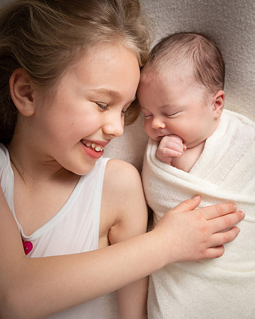 An older sister smiles at and tenderly holds her newborn sister
