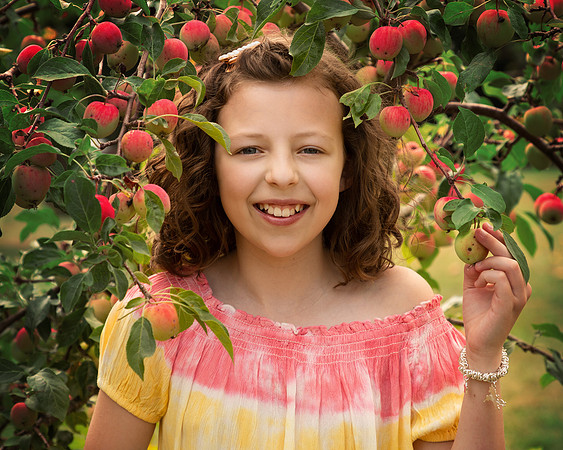 A pre-teen girl smiles surrounded by apples on a tree