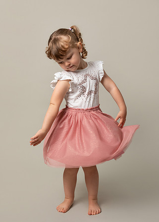 Three-year-old girls spins in a photo studio setting wearing a pink tutu and sparkly top