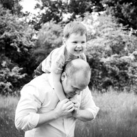 Dad carries son on his shoulders - outdoors, photographed in black & white