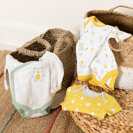 Three baby vests laid out on wicker baskets