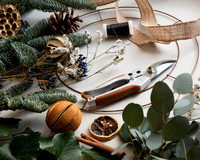 Elements of a wreath-making kit (pine, ribbon, wire, circle, dried orranges, etc) laid out on a white surface