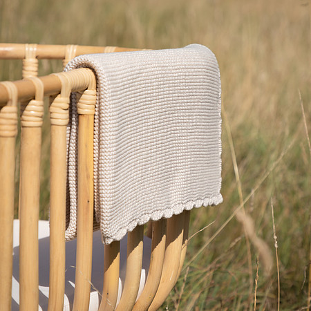 A blanket draped over the edge of a bamboo cot in a field of long grass