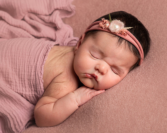 Newborn baby asleep in her front with a pink blanket and headband