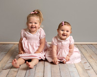 A toddler and her baby sister dressed in matching outfits sitting and smiling