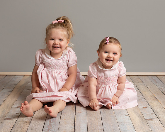 A toddler and her baby sister dressed in matching outfits sitting and smiling