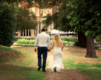 A wedding couple walk away from the camera in the shadow of Windsor's gothic Oakley Court hotel
