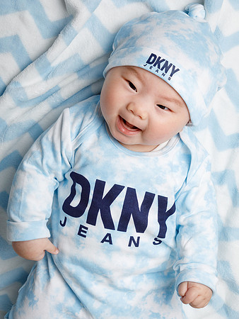 Baby in a DKNY fashion outfit laughs whilst laying on a matching blanket