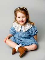 Little girl dressed in denim sits cross legged in a photo studio