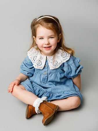 Little girl dressed in denim sits cross legged in a photo studio