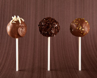 Three chocolate cake pops lined up standing on a brown background