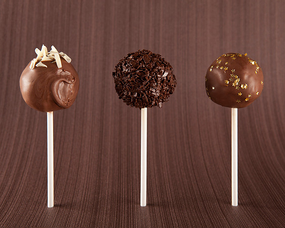 Three chocolate cake pops lined up standing on a brown background