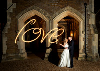 A wedding couple write the word 'love' with sparklers outside the gothic arches of Oakley Court in Windsor