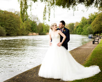 A bride and groom smile at each other by the River Thames in the grounds of Windsor's Oakley Court