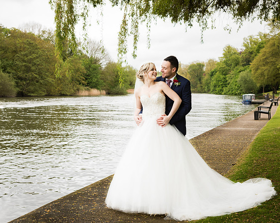 A bride and groom smile at each other by the River Thames in the grounds of Windsor's Oakley Court