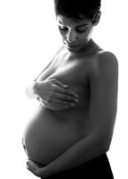 Nude mother cradles her baby bump lit from behind