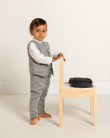 A toddler in a suit stands holding onto a chair