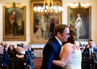 A bride and groom embrace overlooked by their guests and paintings of Royals within Windsor Guildhall's Grand Chamber