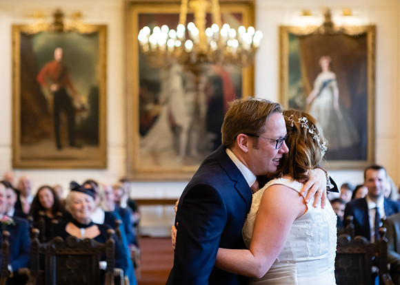 A bride and groom embrace overlooked by their guests and paintings of Royals within Windsor Guildhall's Grand Chamber