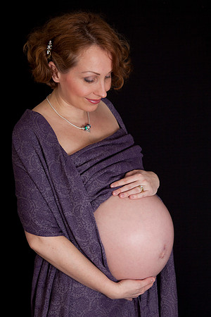 Mum cradles and looks down at her baby bump, draped in purple fabric