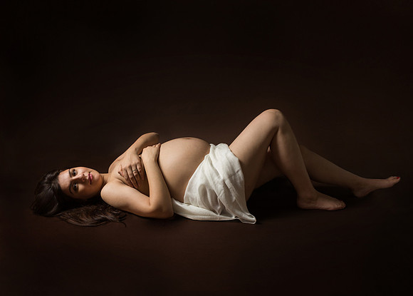 Studio photo of expectant mother laying on her back