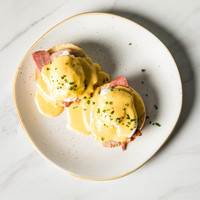 Eggs Benedict photographed from above on a white plate on marble tabletop