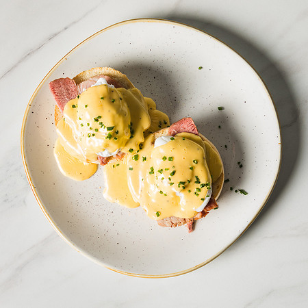 Eggs Benedict photographed from above on a white plate on marble tabletop