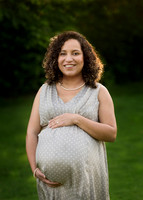 Pregnant mother cradles her baby bump outdoors and smiles for camera