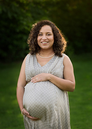 Pregnant mother cradles her baby bump outdoors and smiles for camera