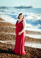 Pregnant mother cradles her baby bump by the sea in Brighton with the pier behind her