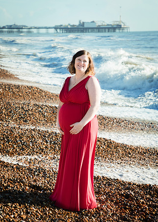 Pregnant mother cradles her baby bump by the sea in Brighton with the pier behind her