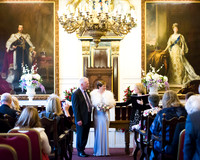 A bride and groom smile at the end of their ceremony in Windsor Guildhall, overlooked by paintings of past Royals