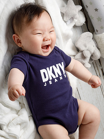Baby wearing a DKNY fashion vest laughs laying on his back
