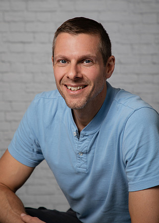 A man smiles at the camera in a relaxed headshot