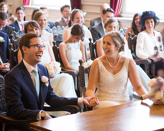 A wedding couple giggle surrounded by their guests inside the Windsor Guildhall