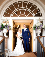 A bride and groom smile for a photo below an arched doorway within Windsor Guildhall