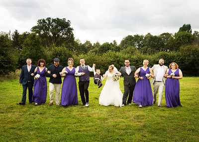 Bridal party walk arm in arm whilst swinging their page boy