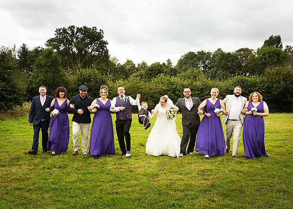 Bridal party walk arm in arm whilst swinging their page boy