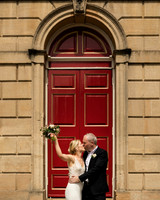 A bride raises her bouquet in the air while kissing her groom in front of the Windsor Guildhall's red doors