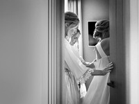 Photo through a doorway or a bride being buttoned into her wedding dress by her bridesmaids