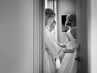 Photo through a doorway or a bride being buttoned into her wedding dress by her bridesmaids