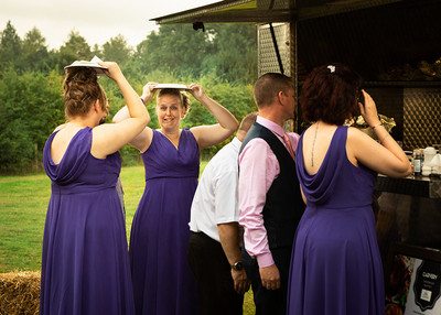 A bridesmaid makes a face whilst queueing for food and sheltering from the rain with a plate over her head