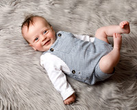 Baby boy lays on a grey fluffy blanket and smiles