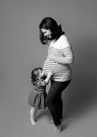 Toddler girl tip toes and kisses her mum's growing baby bump