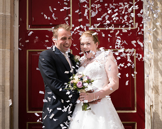 A bride and groom laugh as they are showered with confetti outside Windsor Guildhall